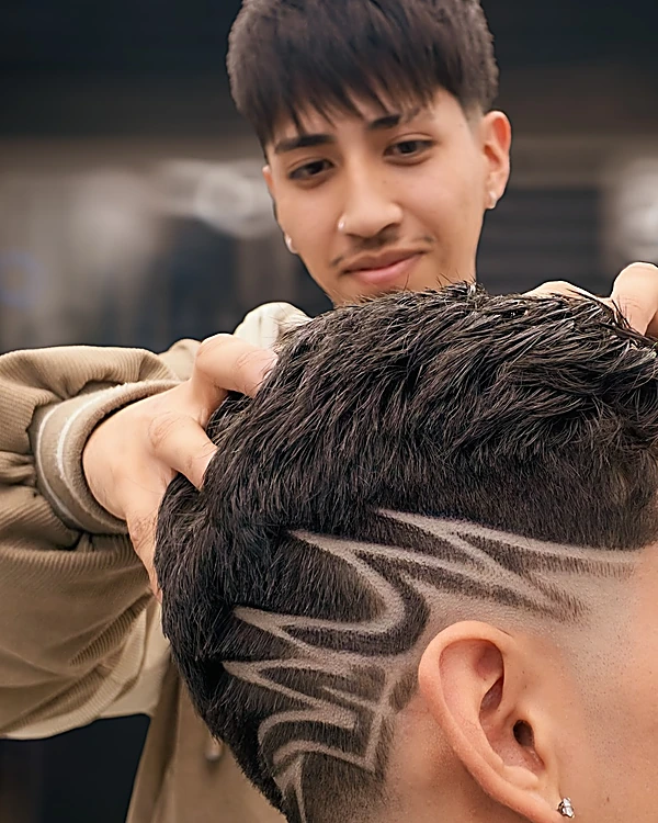 Barbero de Cartel Cuts acomodando el cabello de un cliente, visto de espaldas, con un diseño de líneas curvas rasurado sobre un fade a piel