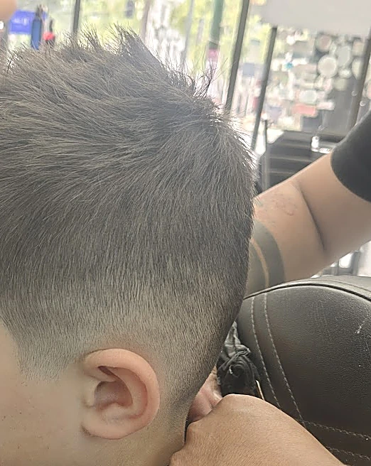 Degradado bajo alrededor de la oreja con el cabello de arriba texturizado, mientras el barbero sostiene la cabeza