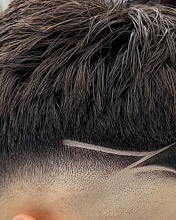 Fade a piel detrás de la oreja con dos líneas rasuradas que se cruzan en el borde del cabello