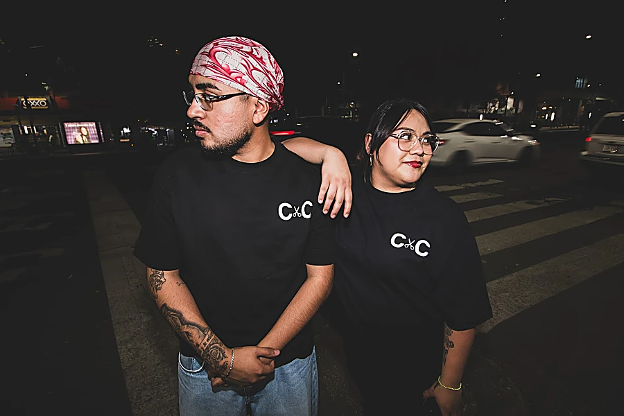 Dos integrantes del equipo con playeras negras C×C, de noche en la calle