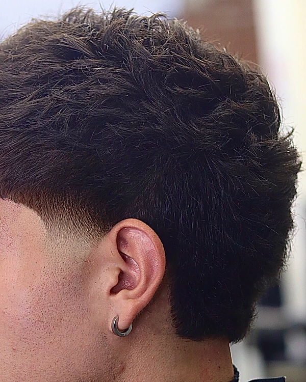 Taper bajo en la patilla y detrás de la oreja, con el cabello de arriba largo y texturizado, visto de lado